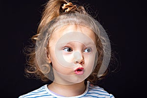 Cute small kid girl with serious face looking and wanting to speek somw words on black studio background. Closeup photo
