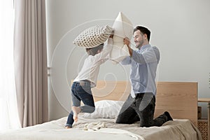 Cute small son playing pillow fight on bed with father