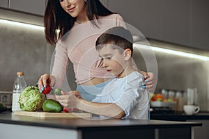 Cute small teen boy helping mother to cook and prepare food in kitchen. Vegetables.