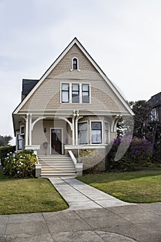 Cute small Victorian house with shingle siding and bay window and flowers in the yard