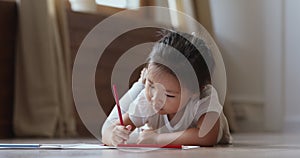 Cute small vietnamese kid girl drawing alone lying on floor