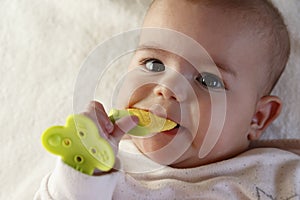 Cute small white skin with brown hair five months baby kid lying on white bed looking up with funny smile on face, holding teether