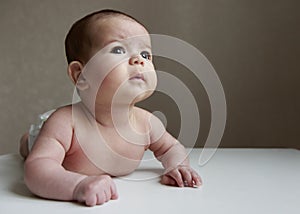 Cute small white skin with brown hair three months baby kid lying on white table looking up with serious face thinking or dreaming