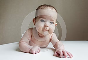 Cute small white skin with brown hair three months baby kid lying on white table looking up with serious face thinking or dreaming