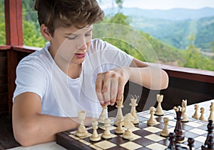 Cute, smart, 11 years old boy in shirt sits in the classroom and plays chess on the chessboard. Training, lesson, hobby,