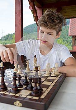 Cute, smart, 11 years old boy in shirt sits in the classroom and plays chess on the chessboard. Training, lesson, hobby, education