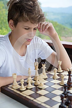 Cute, smart, 11 years old boy in shirt sits in the classroom and plays chess on the chessboard. Training, lesson, hobby, education