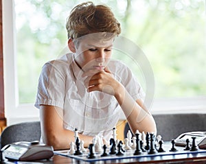 Cute, smart, 11 years old boy in white shirt sits in the classroom and plays chess on the chessboard. Training, lesson, hobby