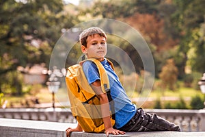 Cute smart boy with backpack sitting outdoors after school.