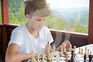 Cute, smart, boy in shirt sits in the classroom and plays chess on the chessboard. Training, lesson, hobby, education concept.