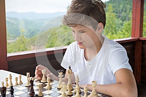 Cute, smart, boy in shirt sits in the classroom and plays chess on the chessboard. Training, lesson, hobby, education concept.