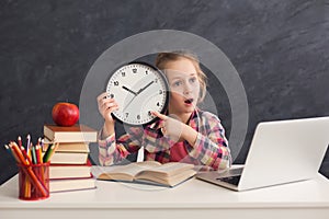 Cute smart girl holding clock and pointing on it