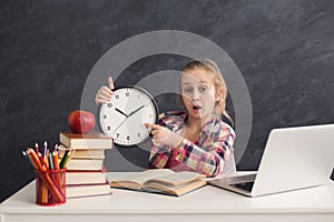 Cute smart girl holding clock and pointing on it