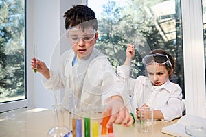 Cute smart kids learning Chemistry in chemical lab. Little children at lesson. Elementary age students doing experiments