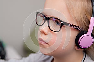 A cute smart little girl wearing eyeglasses, looking at a laptop screen