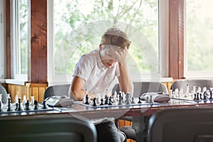 Cute, smart, 11 years old boy in white shirt sits in the classroom and plays chess on the chessboard. Training, lesson, hobby