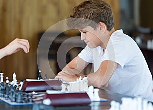 Cute, smart, 11 years old boy in white shirt sits in the classroom and plays chess on the chessboard. Training, lesson, hobby