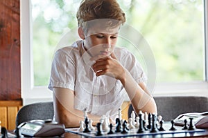 Cute, smart, young boy in white shirt plays chess on the chessboard in the classroom. Education, hobby, training