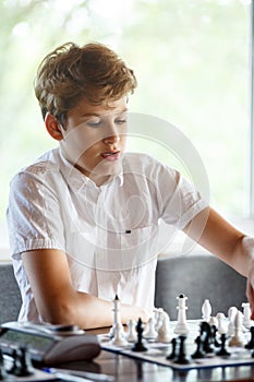 Cute, smart, young boy in white shirt plays chess on the chessboard in the classroom. Education, hobby, training