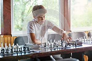 Cute, smart, young boy in white shirt plays chess on the chessboard in the classroom. Education, hobby, training