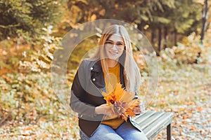 Cute smiley woman holding autumn leaves in fall park. Seasonal, lifestyle and leisure concept.