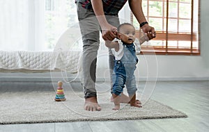 Cute smiling African baby girl learning to walk with father support and holding her hands. Little toddler child taking first steps