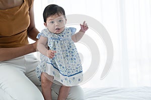 Cute smiling Asian baby girl learning to walk with mother support and holding her body. Happy little toddler child taking first