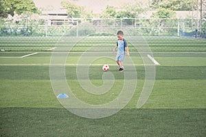 Cute smiling Asian kindergarten boy, football player in soccer uniform is playing football at Training Session, Soccer Drills for