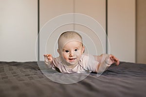 Cute smiling baby boy in bed lying on his belly in bedroom