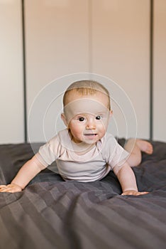 Cute smiling baby boy in bed lying on his belly in bedroom