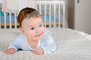 Cute smiling baby boy in bed lying on his belly