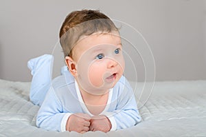 Cute smiling baby boy in bed lying on his belly