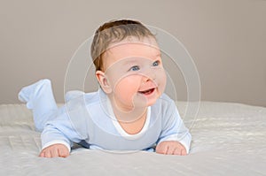 Cute smiling baby boy in bed lying on his belly