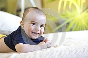 Cute Smiling baby boy with blue T-shirt in white sunny bedroom with green plant.