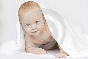 Cute smiling baby boy looking at camera under a white blanket or towel