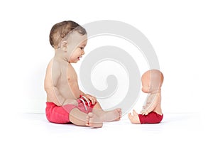 Cute smiling baby boy looks at doll similar to him