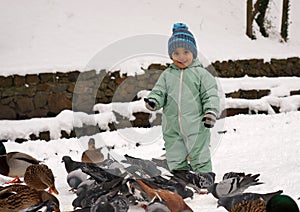 Cute smiling baby boy at the park in winter between birds