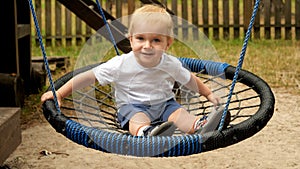 Cute smiling baby boy swinging in rope swing. Kids playing outdoors, children having fun, summer vacation