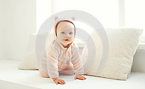 Cute smiling baby crawls in white room home near window