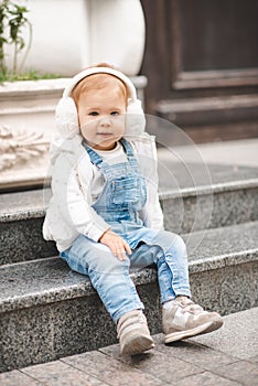 Cute smiling baby girl 1-2 year old wear casual denim pants and white top in city street outdoors. Looking at camera.