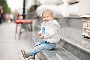 Cute smiling baby girl 1-2 year old wear casual denim pants and white top in city street outdoors. Looking at camera.