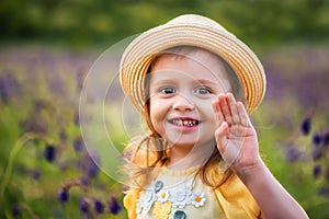 Cute smiling baby girl in beige hat outdoors in green field. Child portrait