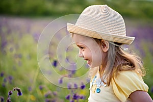 Cute smiling baby girl in beige hat outdoors in green field. Child portrait