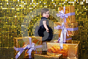 cute smiling baby girl with gift boxes on background with gold shiny sequins, paillettes