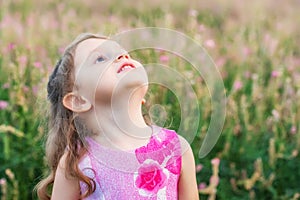 Cute smiling baby girl looks up outdoors in green field. Child portrait