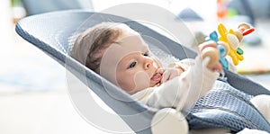 Cute smiling baby laying in bouncer chair. Child playing in a swing.