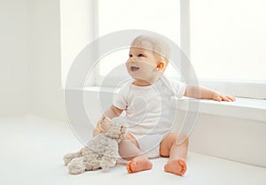 Cute smiling baby with teddy bear toy sitting at home