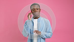 Cute smiling black man, an African American 20 years old in denim shirt, answers phone call, talks to his family on red