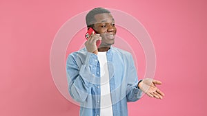 Cute smiling black man, an African American 20 years old in denim shirt, answers phone call, talks to his family on red