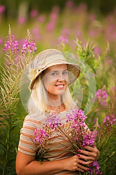 Cute smiling blonde woman with wildflowers. Summer portrait of a woman with rose-tea in the field